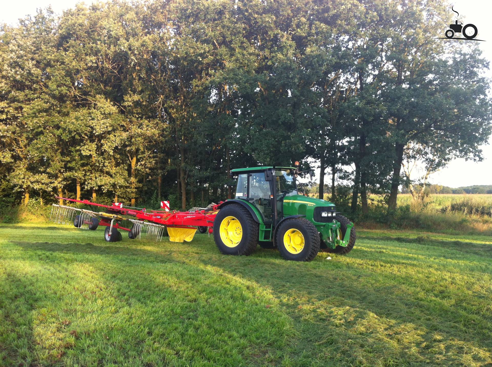 Foto van een John Deere 5100R, bezig met gras harken. Paar uurkes met de demo van Houbraken gewierst